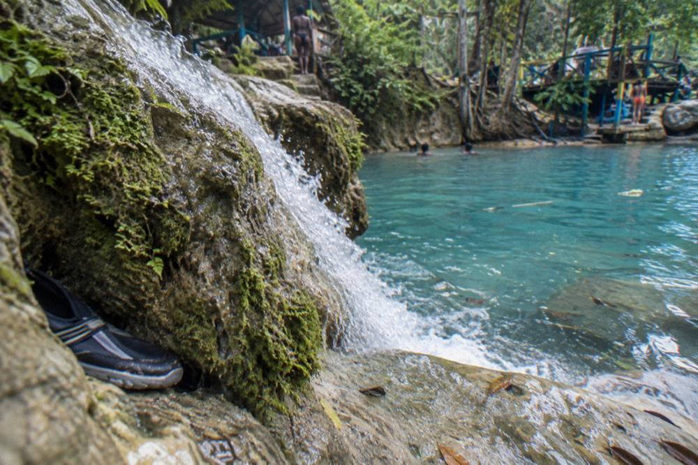 A small waterfall spilling into a clear turquoise pool between mossy limestone rocks