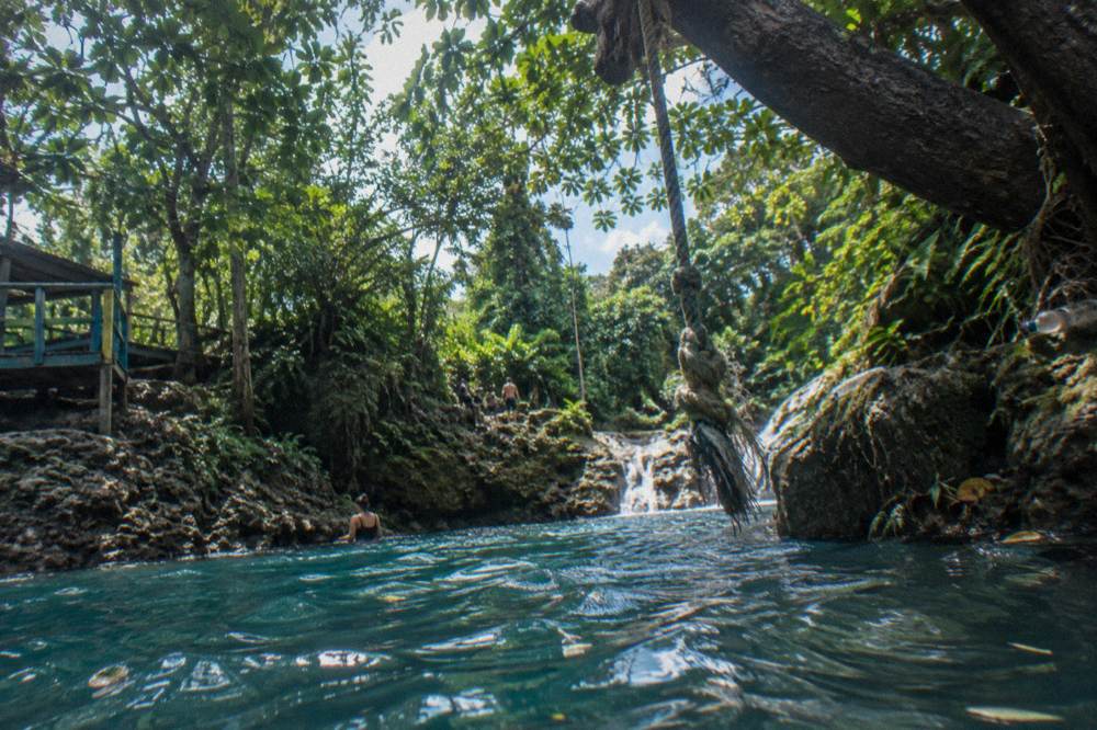 A thick rope swing hanging from a tree over a deep blue jungle pool