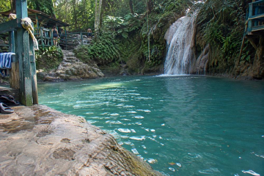Sunlight falling across an empty blue swimming pool below a jungle waterfall in early morning