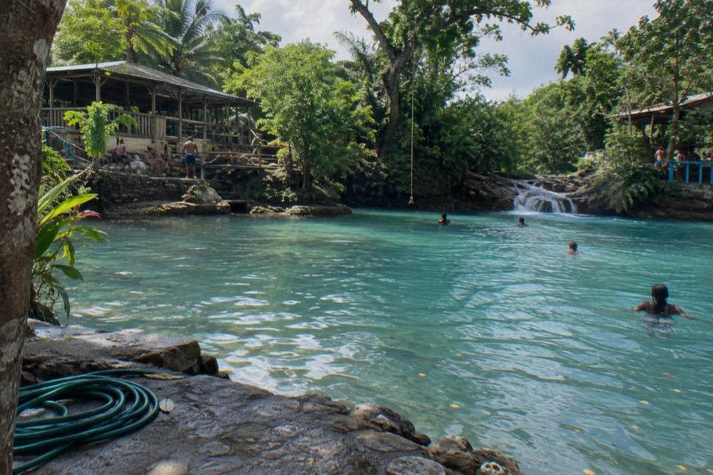 Sunlight over a calm turquoise river pool framed by tropical trees