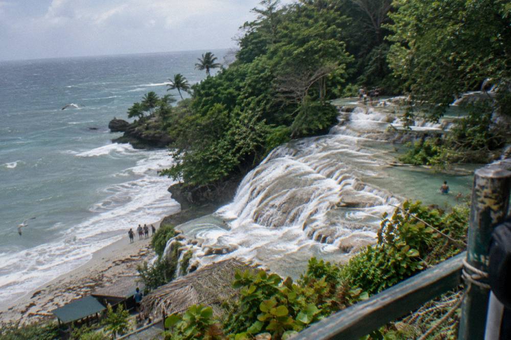 Wide view of a terraced waterfall descending toward the sea near Ocho Rios