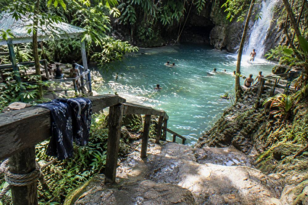 Wooden sign and stone steps leading down to a jungle swimming hole entrance