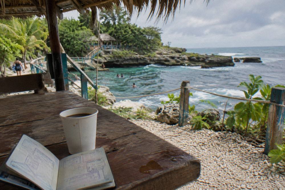 A passport held open beside a laptop on a wooden table in bright daylight