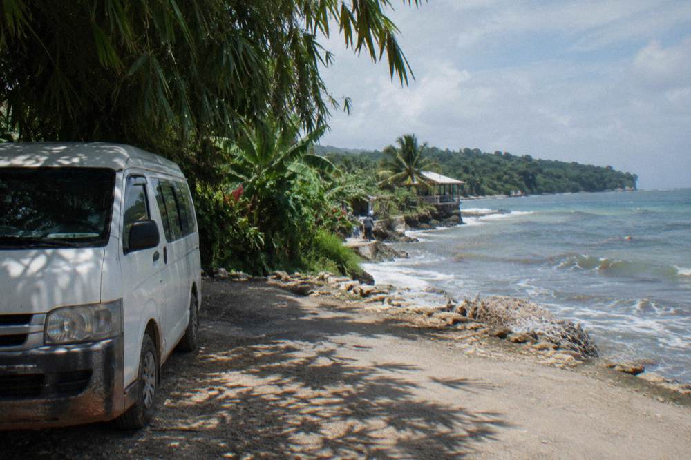 Tour van parked on a rural road beside dense green tropical vegetation