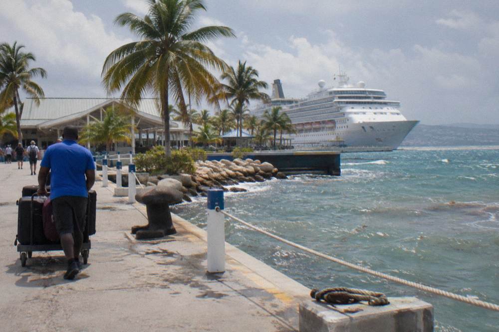 White cruise ship docked at a Caribbean port terminal with palm trees