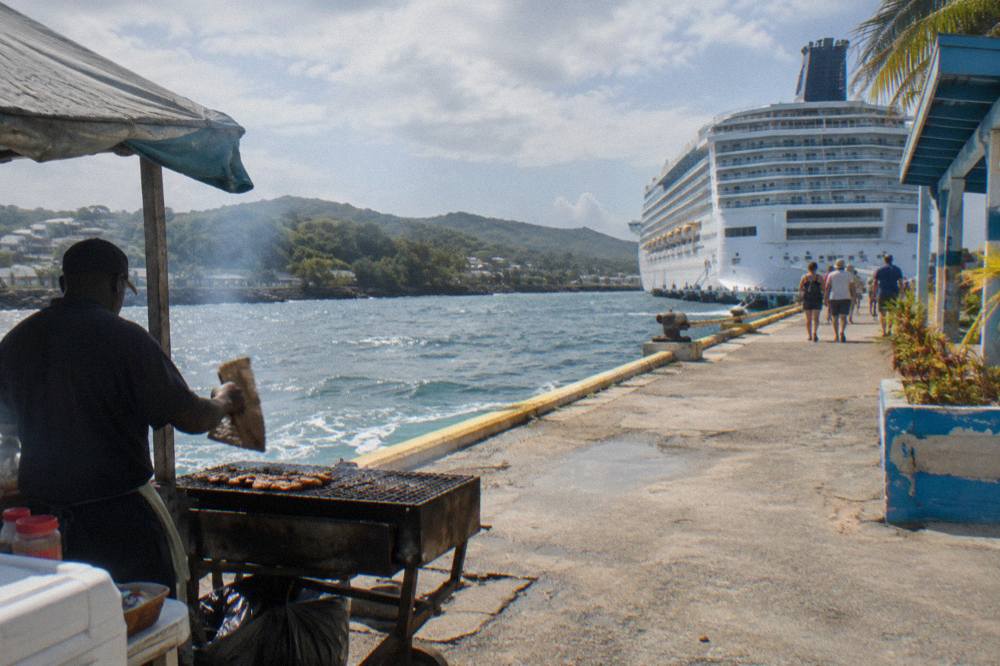 Cruise ship docked at a Caribbean port with tour vans waiting along the pier