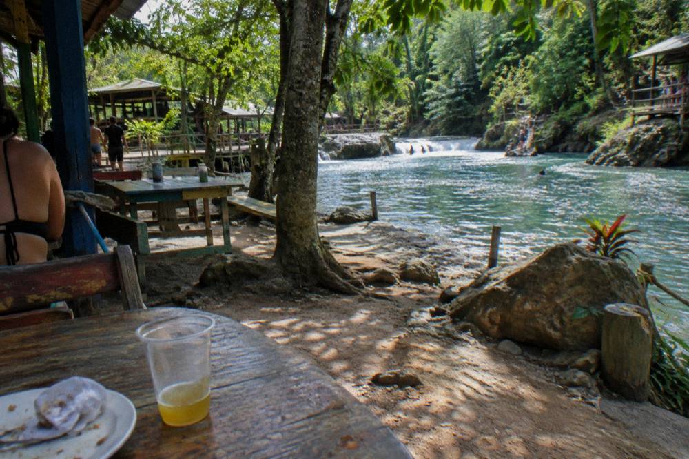 Tables set for an outdoor lunch beside a river with jungle vegetation overhead