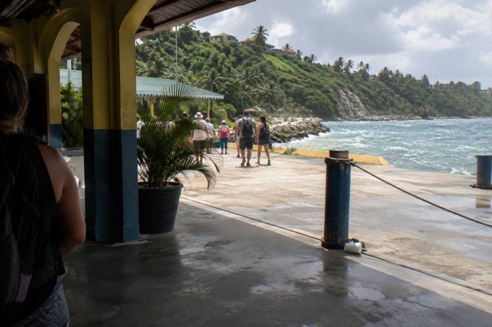 Passengers walking along a cruise ship gangway toward a sunny Caribbean port terminal