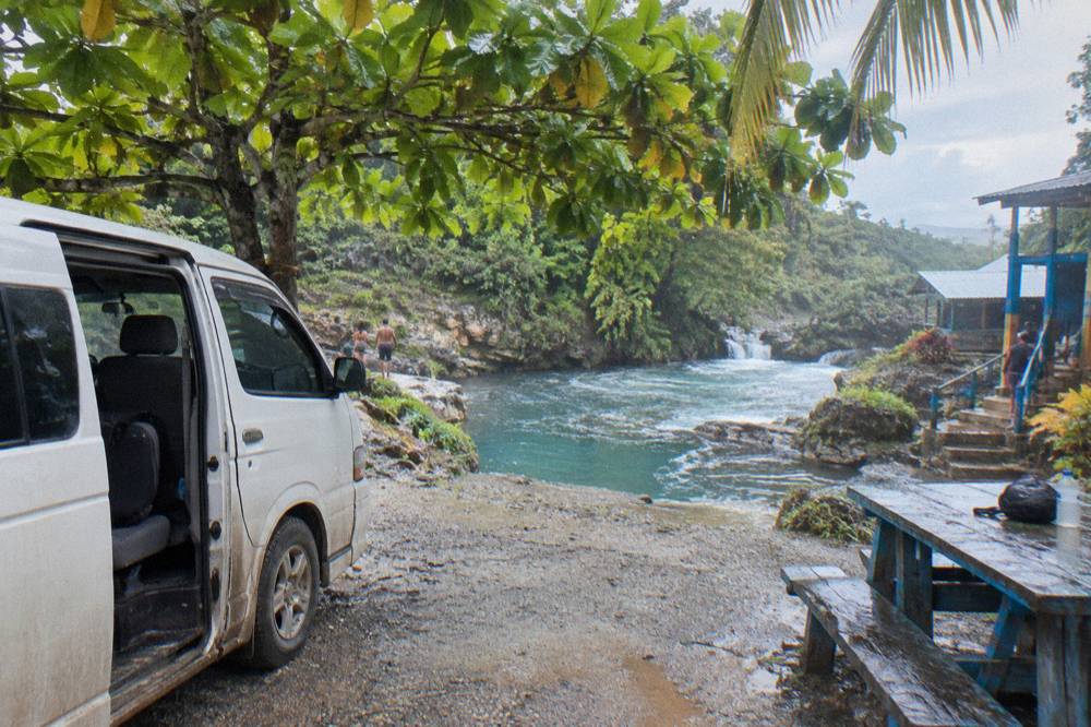 Private minivan parked on a gravel road beside tropical vegetation