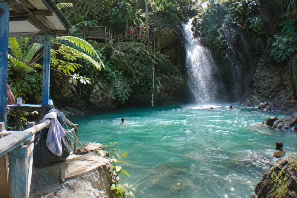 Sunlight falling on a turquoise pool at the base of a jungle waterfall