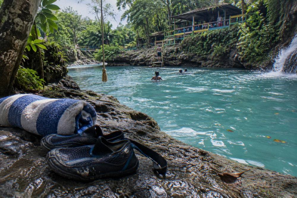 Water shoes and a rolled towel on a rock beside a turquoise jungle pool