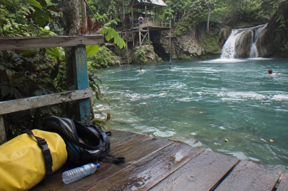 Dry bag and packed daypack resting on a bench beside a jungle trail