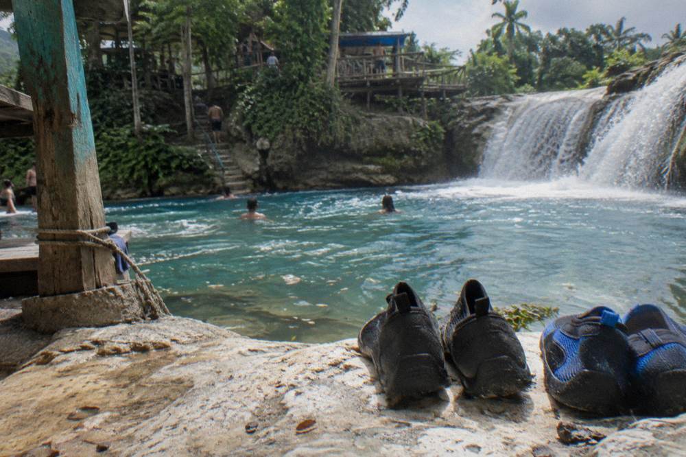 Pair of water shoes drying on a sunlit limestone ledge next to a waterfall pool