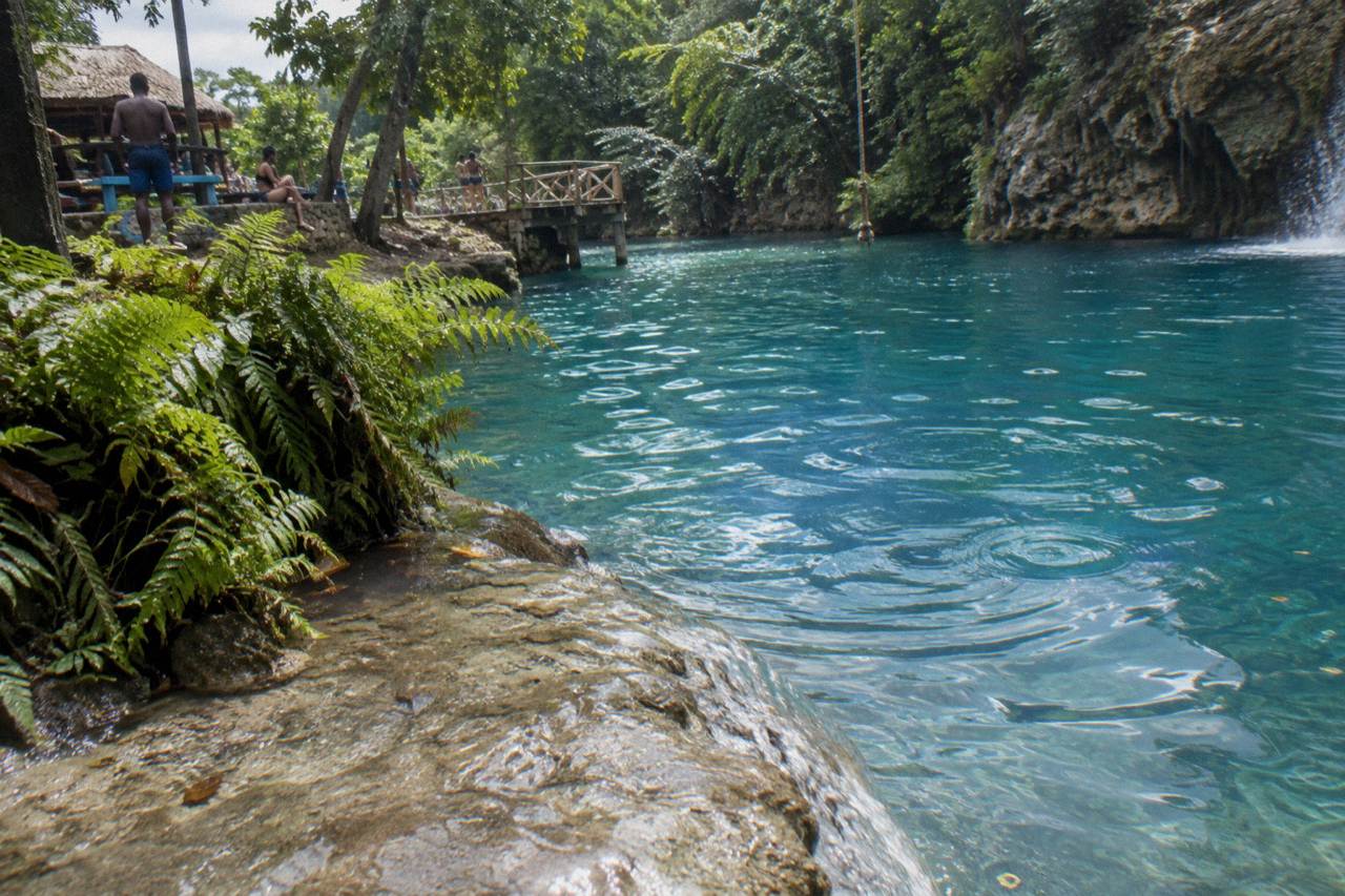 Clear turquoise pool at the base of a jungle waterfall surrounded by ferns and limestone rock