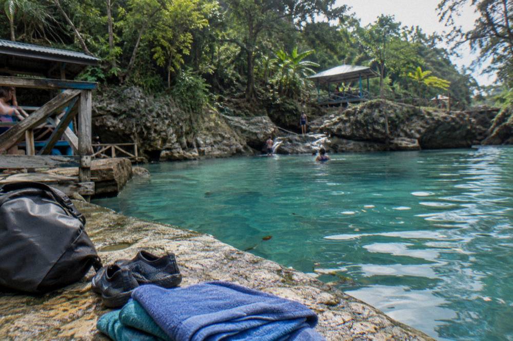 Water shoes, dry bag and towels set on a rock beside a calm turquoise pool